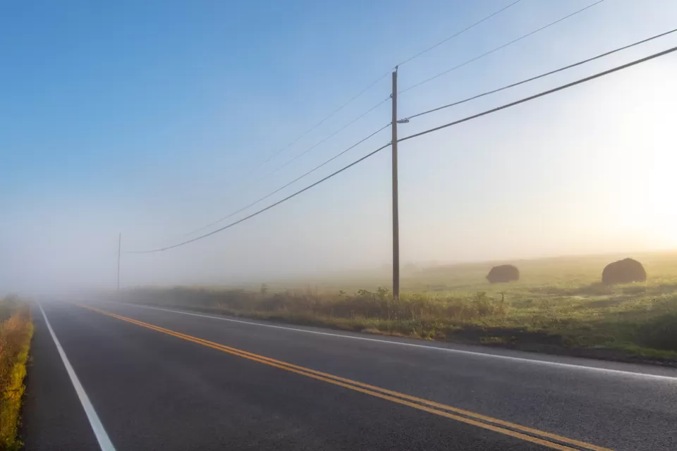 Foggy rural road with power lines and haystacks along the side